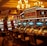 A casino floor featuring rows of brightly lit video poker machines. The area is illuminated by elegant chandeliers, with a display board showing a large sum of money, suggesting a possible jackpot. The rich decor includes luxurious carpets and comfortable seating, adding to the opulent atmosphere.