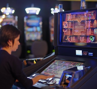 A person is seated at a slot machine console in a casino, focusing intently on the game displayed on the screen. The background shows several other illuminated gaming machines, adding a vibrant and colorful atmosphere to the scene.